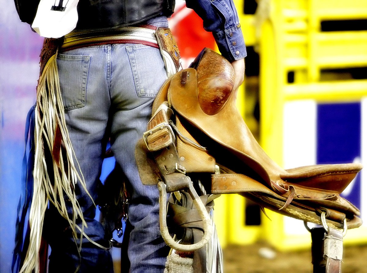The backside of a rodeo saddle bronc cowboy as he carries his saddle before a competition