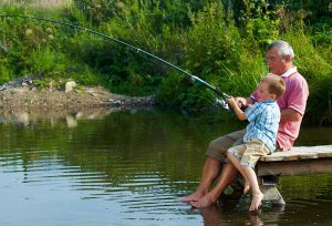 photo-of-grandfather-and-grandson-sitting-on-pontoon-with-their-feet-in-water-and-fishing-on-weekend