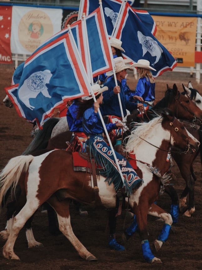 Flag girls on horseback carrying Wyoming Flags at Cody Nites Rodeo