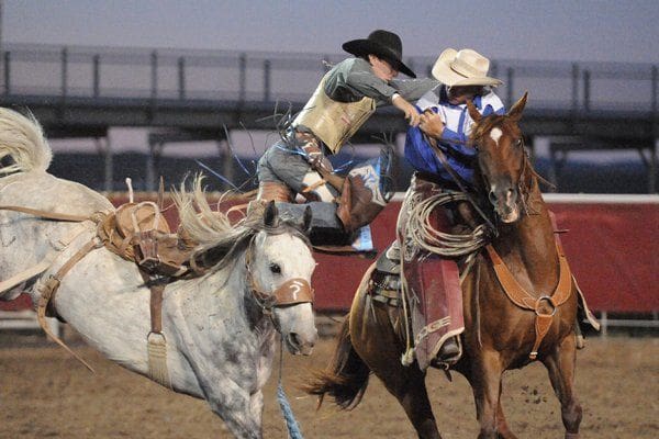 Cowboy dismounting off a saddle bronc onto a pick up man's horse