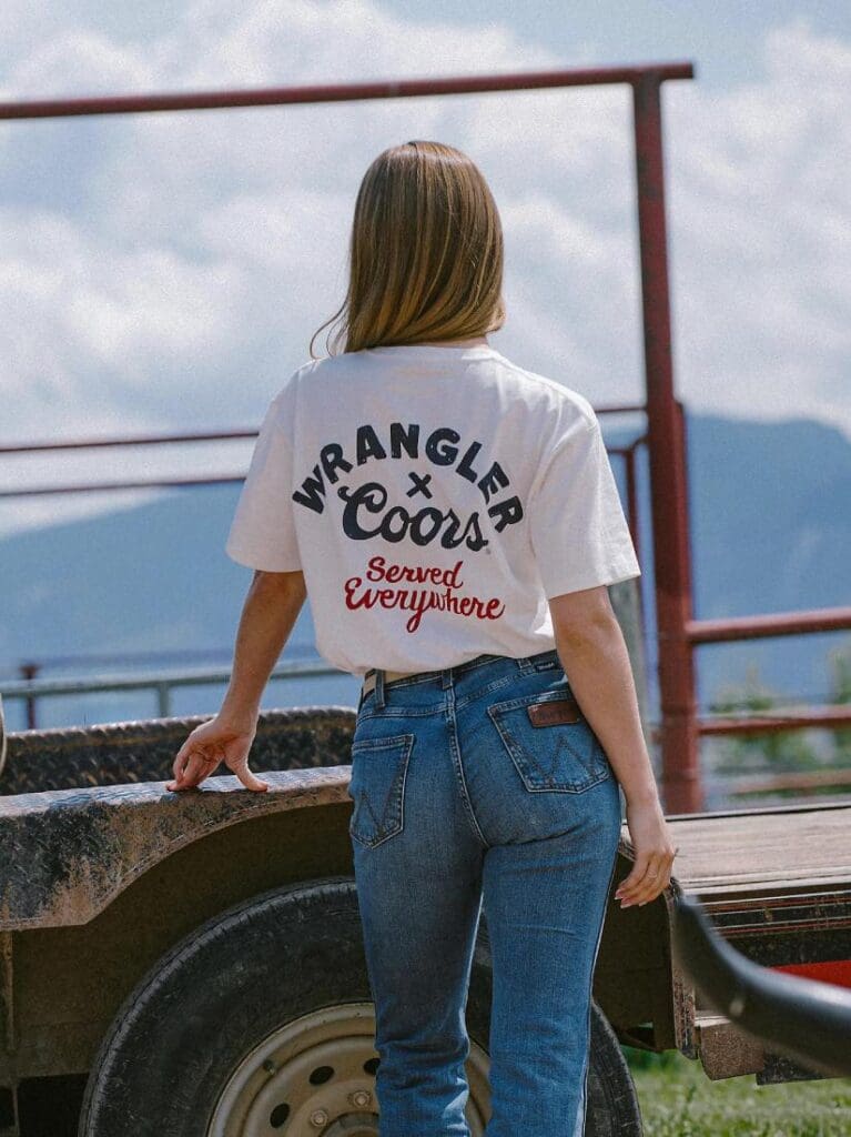 Woman wearing Wrangler Jeans and Wrangler Coors Served Everywhere T-Shirt standing by a trailer.