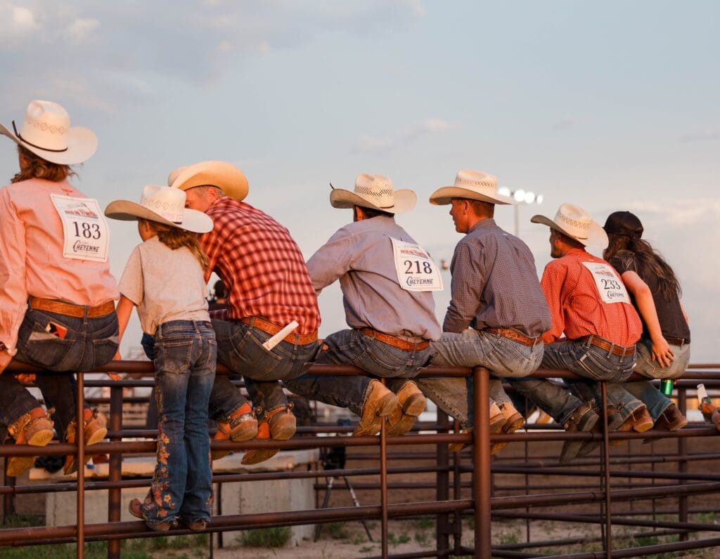 Rodeo competitors and fans sitting on arena fence