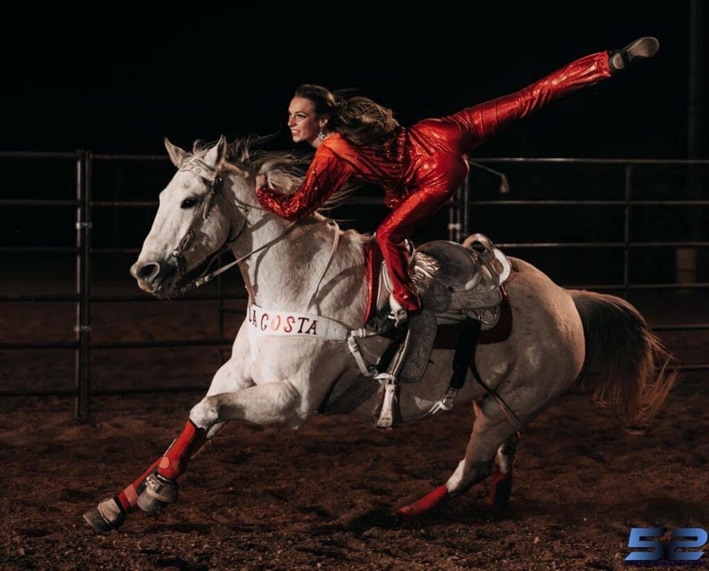 Trick rider balancing on one leg on top of a horse.