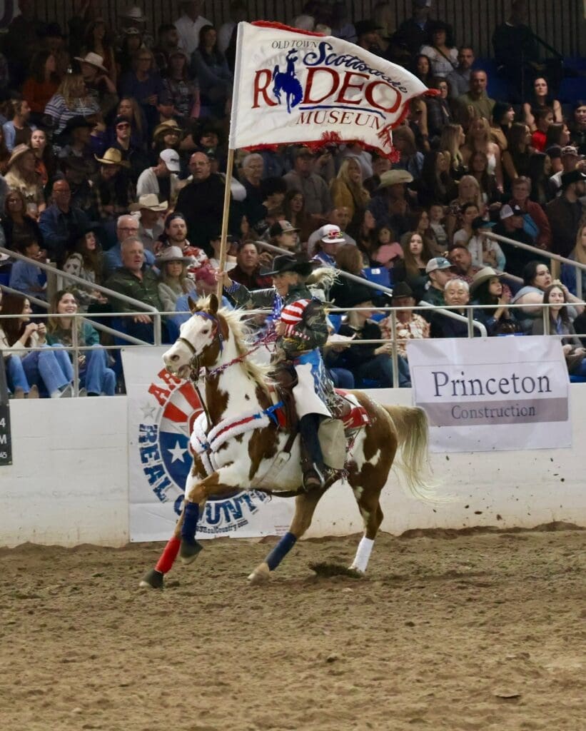 Cowgirl carrying the Scottsdale Museum flag in arena at Rodeo Scottsdale