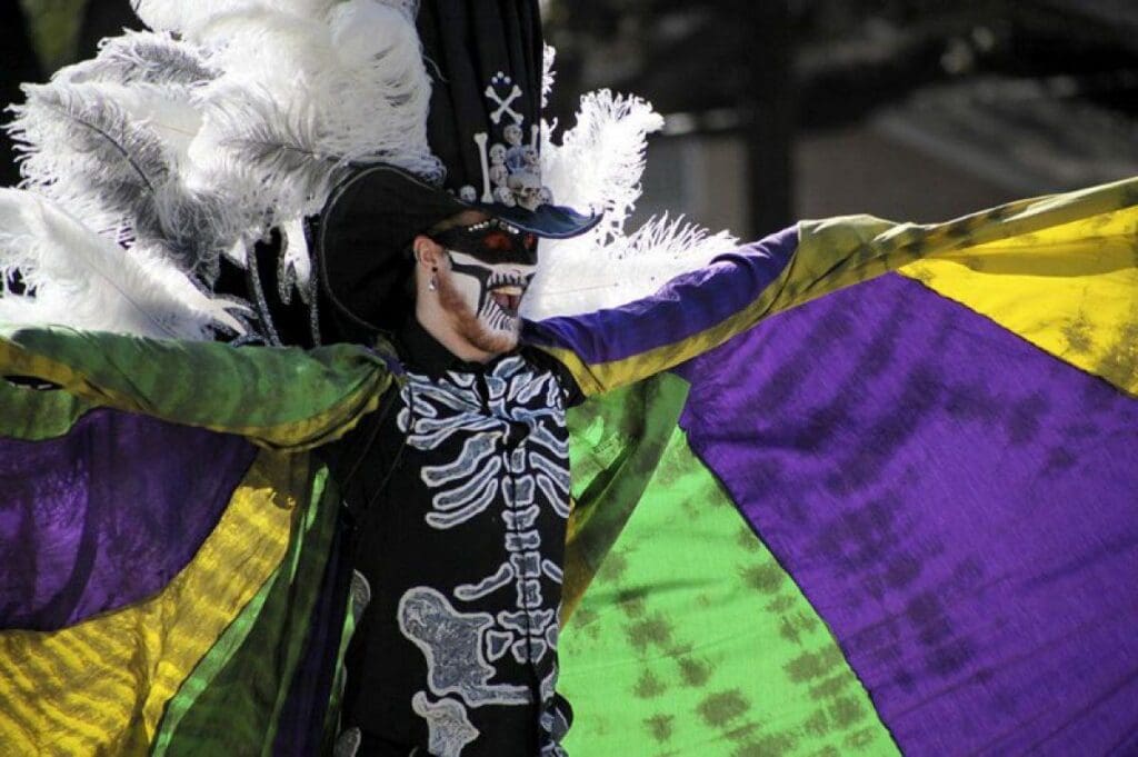 Mardi Gras parade member dressed in a skeleton costume with a vibrant cape of green, gold and purple. Photo credit: mardigrasneworleans.com
