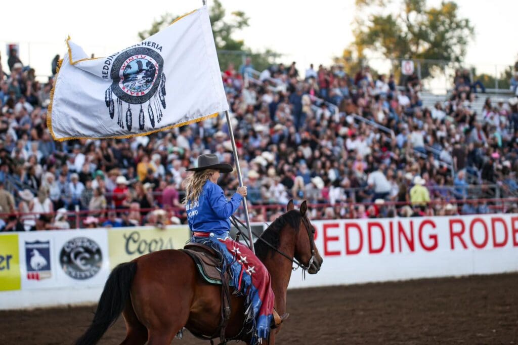 Cowgirl carrying a Redding Rancheria flag in the Redding Rodeo arena