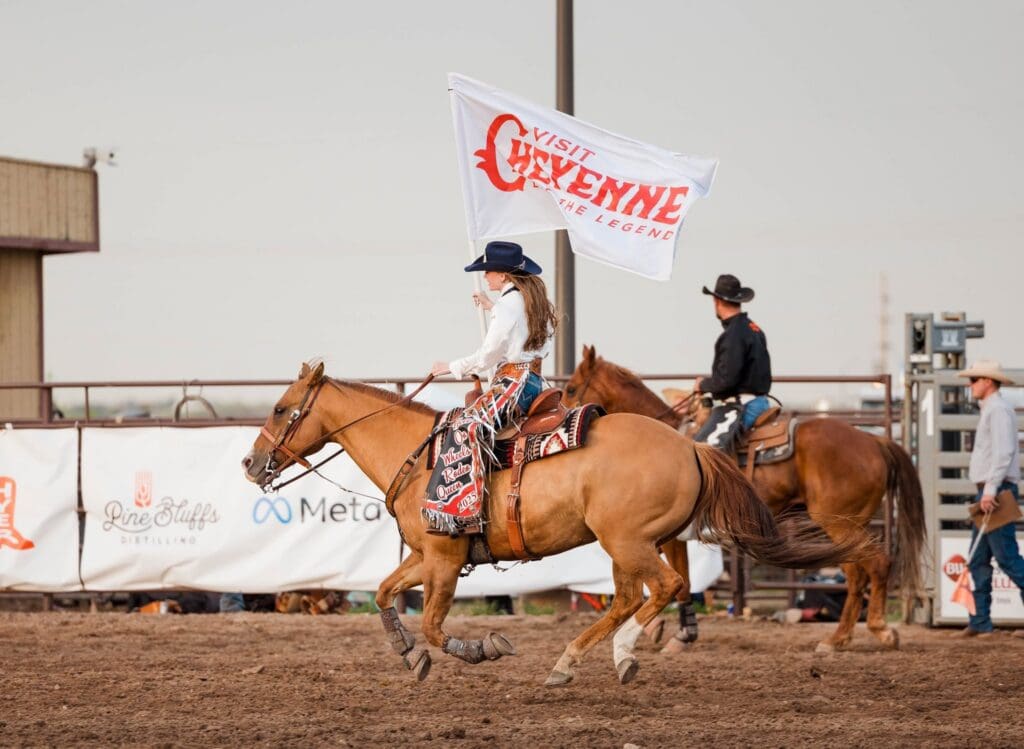 Rodeo Queen carrying a Visit Cheyenne flag in the arena