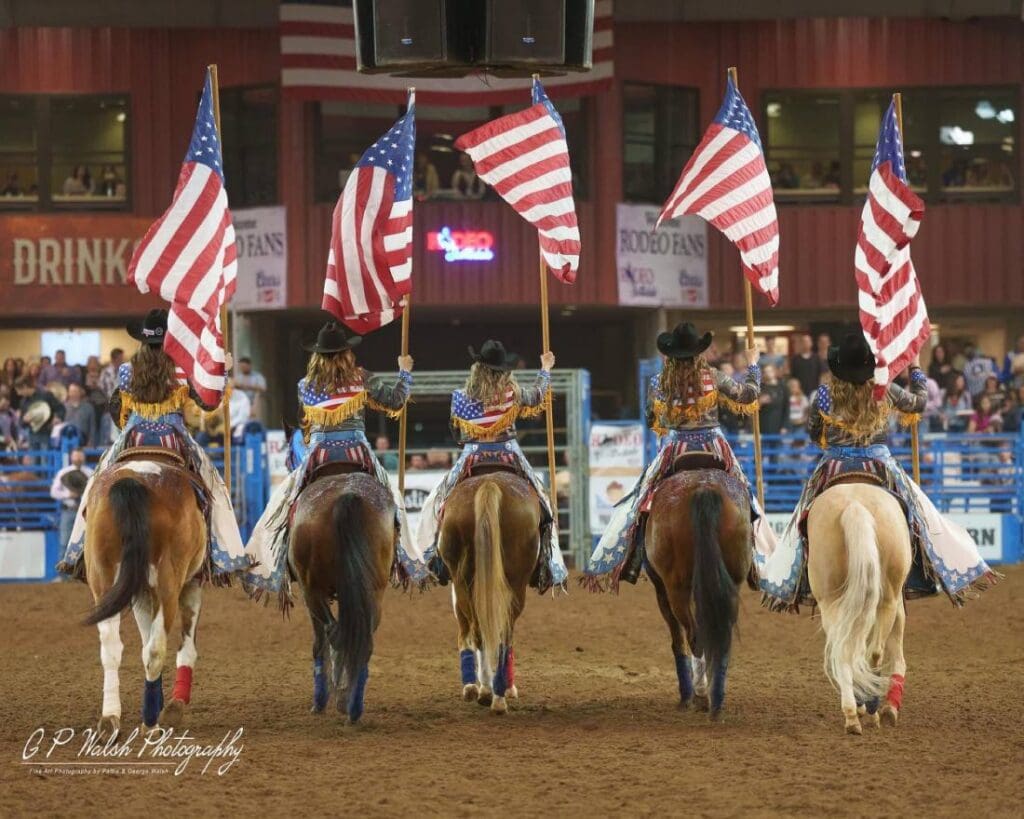 American flag presented on horseback of 5 cowgirls.  View from the back.  GP Walsh Photography from Rodeo Scottsdale fb